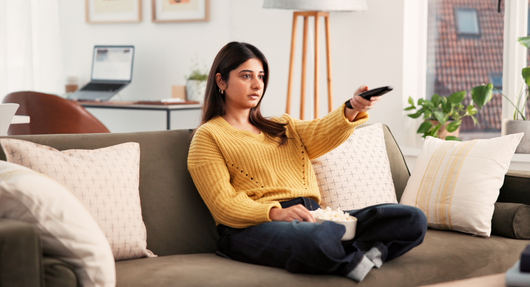 A woman on the couch with a TV remote and popcorn.