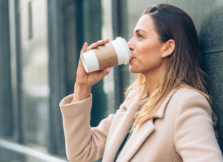 A woman drinking out of a travel coffee cup.