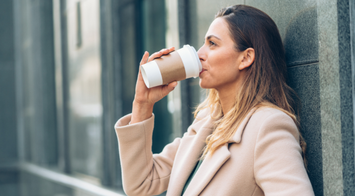 A woman drinking out of a travel coffee cup.