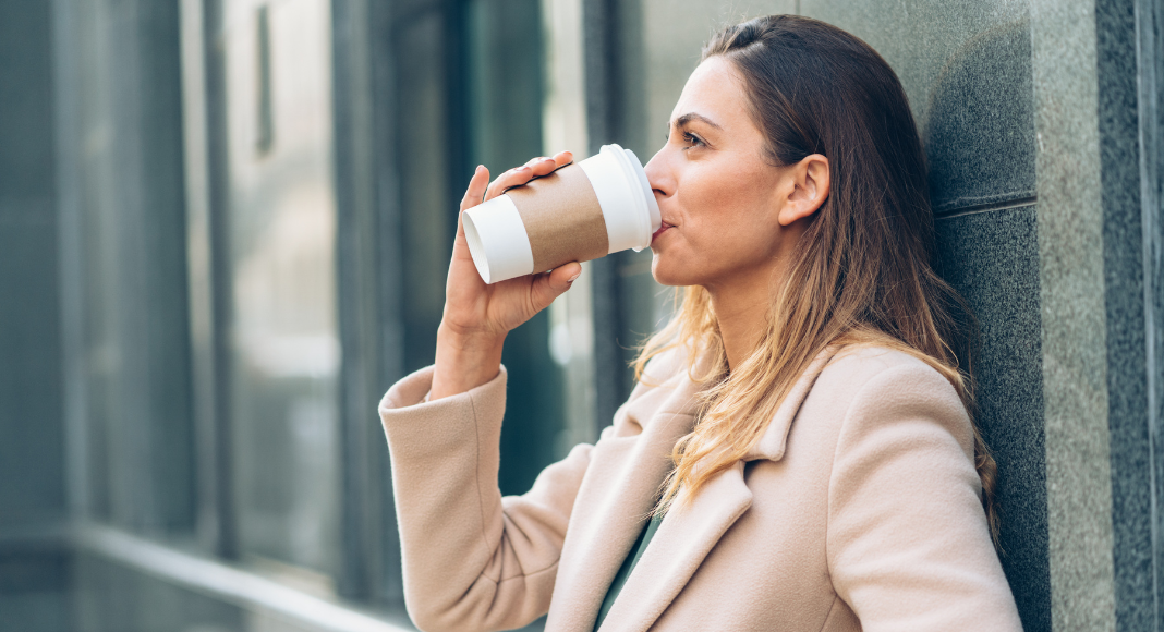 A woman drinking out of a travel coffee cup.