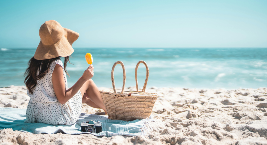 A woman sitting on the beach eating a Popsicle.