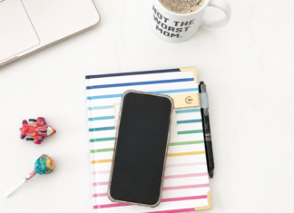 A phone placed on an agenda book next to a computer and coffee.